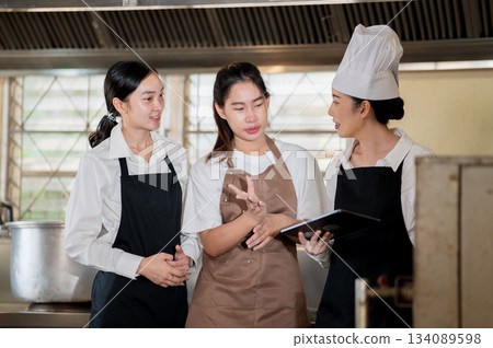 Asian female chef holding tablet and talking to students in front of a stove or oven in the kitchen 134089598