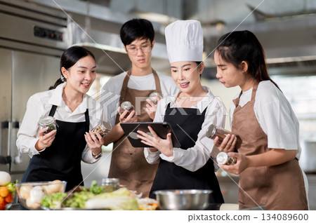 Asian female chef holding tablet showing cooking recipe to her students with seasonal jars in hands. 134089600