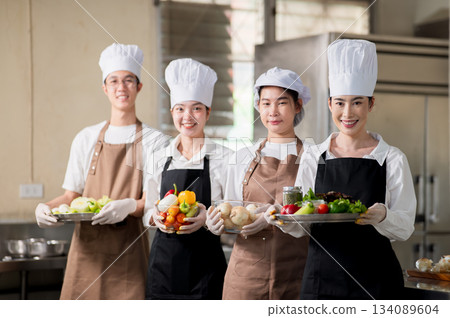 Asian chefs wearing gloves and apron holding stainless plate and glass bowl full of fresh vegetables Asian chefs wearing gloves and apron holding stainless plate and glass bowl full of fresh vegetables 134089604