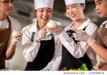 Close up of gloved hands female chef holding a peeled onion with students pointing their fingers. Close up of gloved hands female chef holding a peeled onion with students pointing their fingers. 134089616