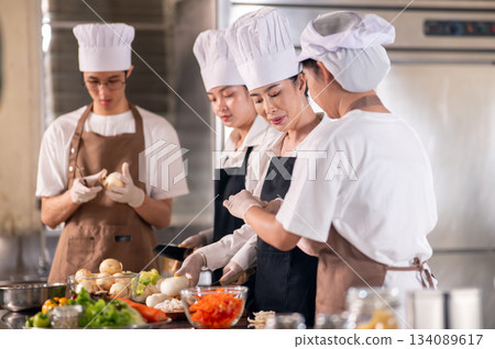 Asian female chef is looking at her students or assistant peeling onions at kitchen cooking counter. Asian female chef is looking at her students or assistant peeling onions at kitchen cooking counter. 134089617