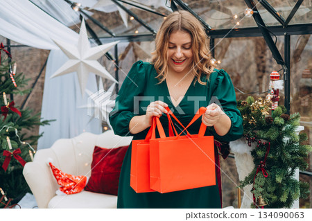 Middle age Caucasian woman in dress smiling confident holding Christmas gift bag at home. Winter time and holidays. Celebration banner, big sale concept Middle age Caucasian woman in dress smiling confident holding Christmas gift bag at home. Winter time and holidays. Celebration banner, big sale concept 134090063