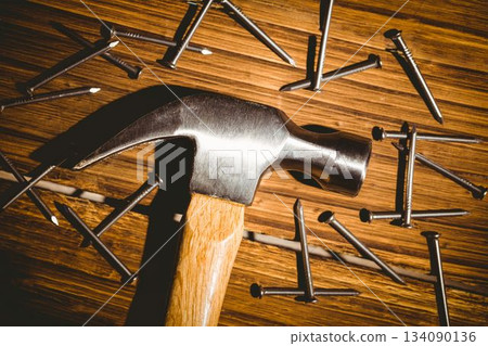 Claw hammer is lying flat on wood-grain work surface with scattered steel nails, flat design Claw hammer is lying flat on wood-grain work surface with scattered steel nails, flat design 134090136