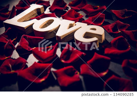 Wooden letters spelling love are resting in 3D render on dark matte surface with red petals 134090285