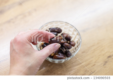 Hand picking dried date fruit from glass bowl Hand picking dried date fruit from glass bowl 134090503
