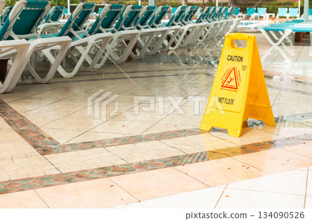 Warning sign caution wet floor among pool deck chairs near the hotel swimming pool Warning sign caution wet floor among pool deck chairs near the hotel swimming pool 134090526