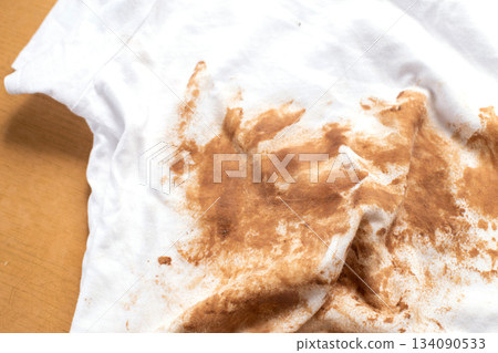 Dirty stains covering white t-shirt lying on wooden table Dirty stains covering white t-shirt lying on wooden table 134090533