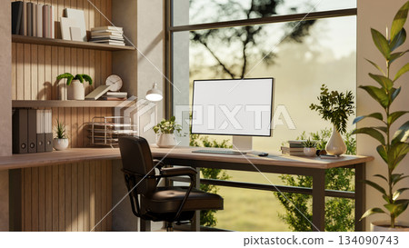 Blank screen computer on a wooden table and armchair near glass wall with nature view outside. 134090743