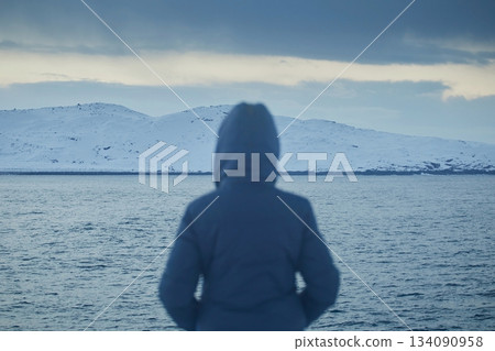 A girl in a blue jacket against the background of a non-freezing sea and a ship in winter, blurry focus, visible on the silhouette 134090958