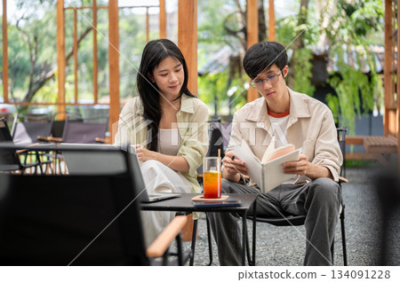 Asian woman is looking or reading a notebook in a man hands while sitting together at folding table. Asian woman is looking or reading a notebook in a man hands while sitting together at folding table. 134091228