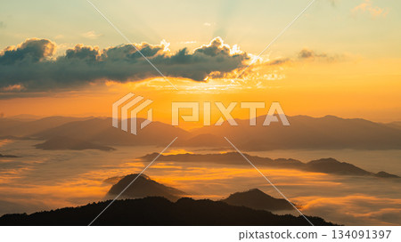 Serene Sunrise Over Mountain Range with Layers of Mist and Golden Light Illuminating the Sky and Welcoming a New Day in Nature's Beauty Serene Sunrise Over Mountain Range with Layers of Mist and Golden Light Illuminating the Sky and Welcoming a New Day in Nature's Beauty 134091397
