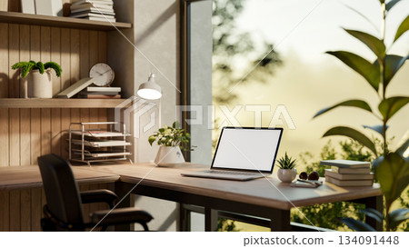 Blank screen laptop on a wooden table and armchair in a glass wall room with nature view outside. 134091448
