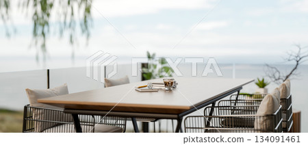 A coffee cup and glasses over book on wooden dining table with armchairs at cafe balcony or rooftop. A coffee cup and glasses over book on wooden dining table with armchairs at cafe balcony or rooftop. 134091461