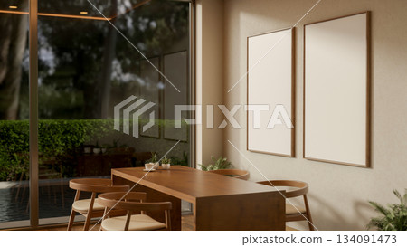 A coffee cup on wooden table and armchairs in a room with blank frame hanging on a cafe or shop wall 134091473