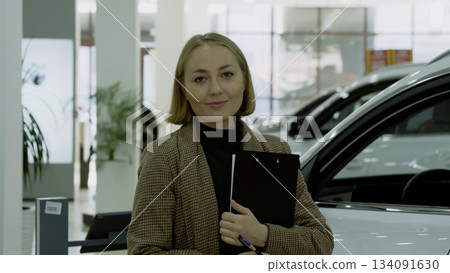 Young female sales agent holding documents near a new car in the showroom Young female sales agent holding documents near a new car in the showroom 134091630