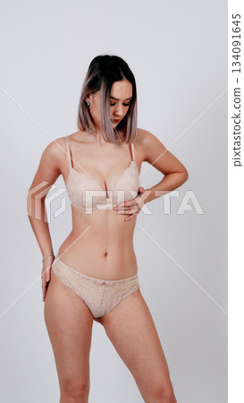 Female model posing in nude-colored lingerie set and briefs Female model posing in nude-colored lingerie set and briefs 134091645