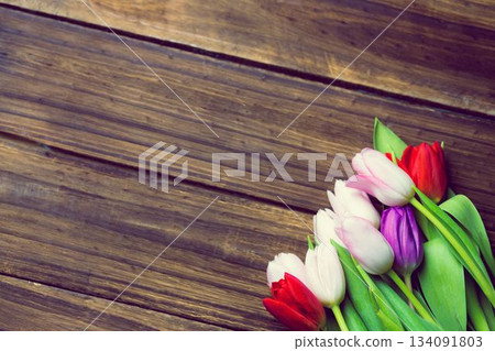 Showing flat design multicolor tulips with green leaves lying diagonally over rustic wooden planks Showing flat design multicolor tulips with green leaves lying diagonally over rustic wooden planks 134091803