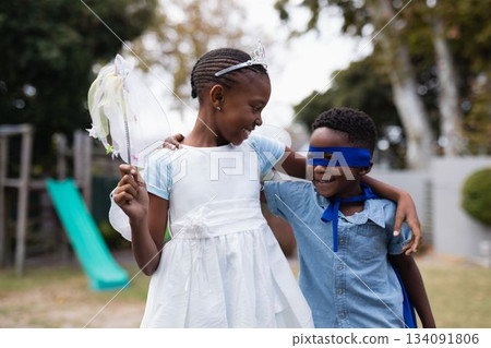 African american siblings wearing angel and superman costumes smiling and standing in park African american siblings wearing angel and superman costumes smiling and standing in park 134091806