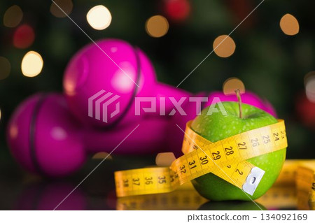 Vector art is showing green apple wrapped in yellow tape with pink dumbbells amid golden bokeh 134092169