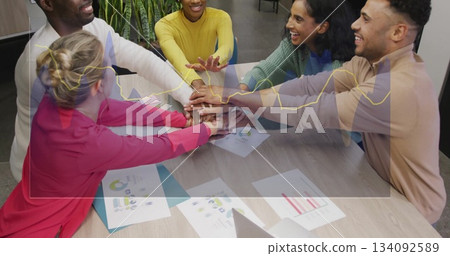 Colleagues wearing tops stacking hands in office meeting room, with laptop charts and graphs Colleagues wearing tops stacking hands in office meeting room, with laptop charts and graphs 134092589