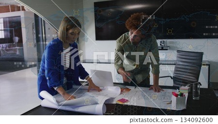 Leaning architects reviewing blueprints on table in office meeting room, with laptop, sticky notes Leaning architects reviewing blueprints on table in office meeting room, with laptop, sticky notes 134092600
