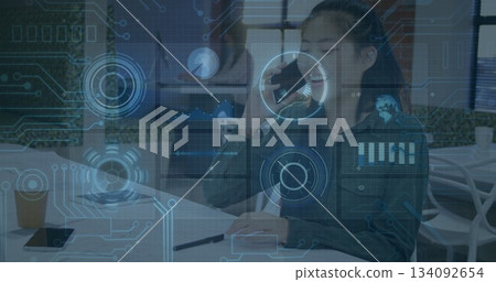 Asian businesswoman holding smartphone and writing in notebook at office table, with coffee cup 134092654