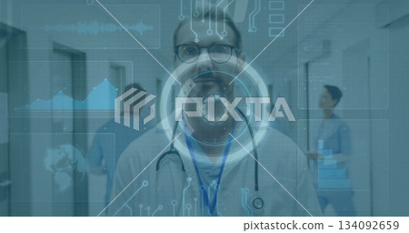 Standing doctor in white lab coat with blue lanyard presenting HUD overlay in hospital corridor Standing doctor in white lab coat with blue lanyard presenting HUD overlay in hospital corridor 134092659