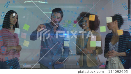 Team in suits collaborating at glass board with sticky notes and tablet in meeting room Team in suits collaborating at glass board with sticky notes and tablet in meeting room 134092695