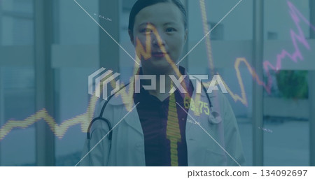 Standing Chinese doctor wearing white coat and stethoscope in hospital, with line graph overlay Standing Chinese doctor wearing white coat and stethoscope in hospital, with line graph overlay 134092697