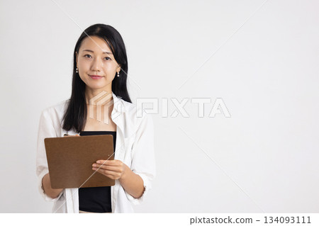 一位面帶微笑的女子手裡拿著一個活頁夾和一支筆。 134093111