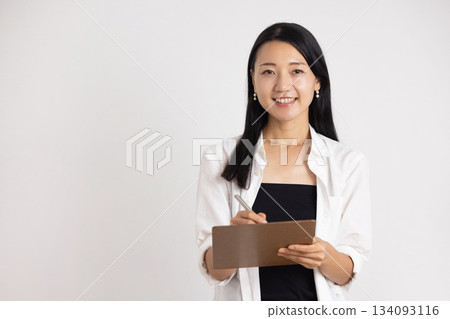 一位面帶微笑的女子手裡拿著一個活頁夾和一支筆。 134093116