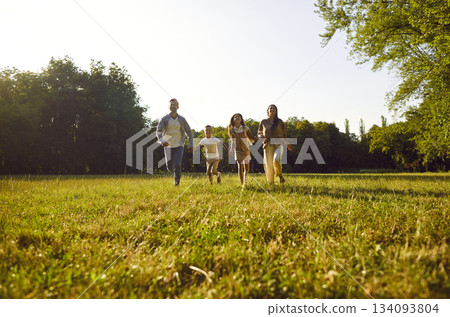 Happy family with two kids running on green grass and having fun in summer park at sunset. 134093804