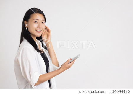 一位戴著無線耳機的女士一邊看著她的智慧型手機一邊微笑。 134094430