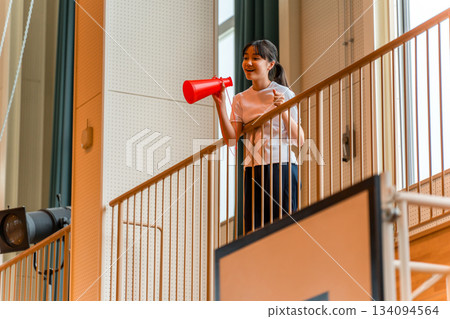 A female student in gym clothes cheering with a megaphone in the gym (cheer, cheer, do your best) 134094564