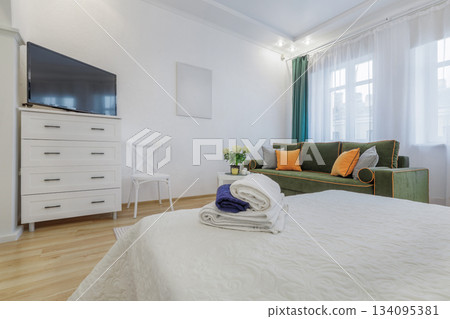 Bright Cozy Room with Green Sofa and Fresh Towels on Bed 134095381