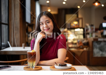Young asian woman resting head on hand sitting with orange coffee aside cake on table in the cafe. 134095463