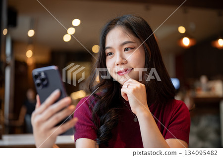 Close up pretty asian woman holding looking at smartphone resting head on hand while sitting in cafe 134095482