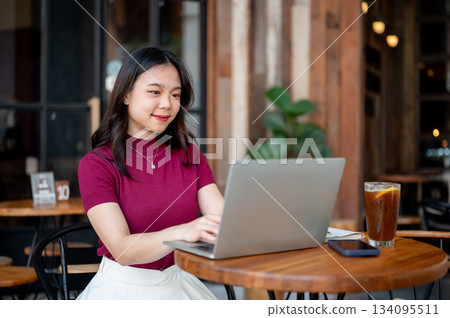 Asian woman looking and working on laptop aside phone and coffee while sitting at cafe's table 134095511