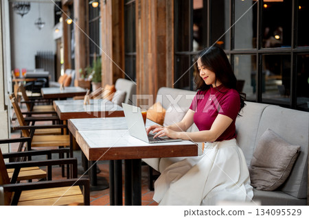 Pretty asian woman typing or looking at laptop on marble table sitting at sofa in an open air cafe. Pretty asian woman typing or looking at laptop on marble table sitting at sofa in an open air cafe. 134095529