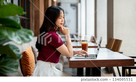 Pretty asian woman resting head on hand looking at laptop on marble table sitting on sofa in a cafe. Pretty asian woman resting head on hand looking at laptop on marble table sitting on sofa in a cafe. 134095531