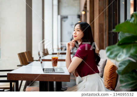 Pretty asian woman resting head on hand looking away from laptop on table sitting on sofa in a cafe. 134095532