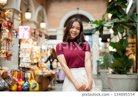 Asian woman tourist customer standing beside a souvenir cart in an indoor market or shopping mall. Asian woman tourist customer standing beside a souvenir cart in an indoor market or shopping mall. 134095554