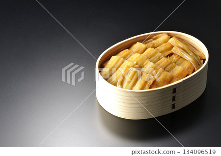 一個盛有煮熟康吉鰻的便當盒,在黑色背景下拍攝的照片。 一個盛有煮熟康吉鰻的便當盒,在黑色背景下拍攝的照片。 134096519