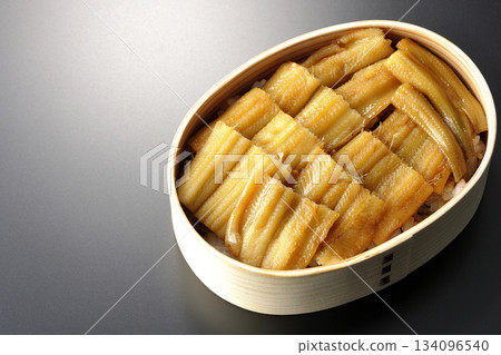 一個盛有煮熟康吉鰻的便當盒，在黑色背景下拍攝的照片。 134096540