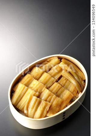 一個盛有煮熟康吉鰻的便當盒，在黑色背景下拍攝的照片。 134096549