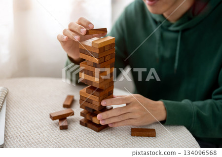 Close up a man's hand putting a piece on top of wooden block toy tower playing alone on round table 134096568