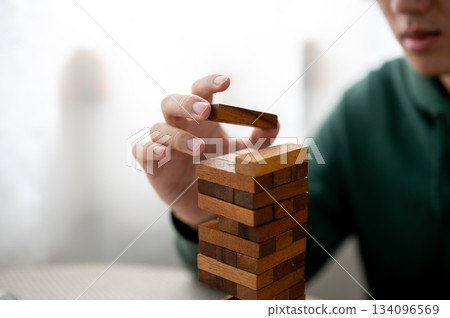 Close up man's hand putting a piece on top of wooden blocks in tower building game as playing alone. 134096569