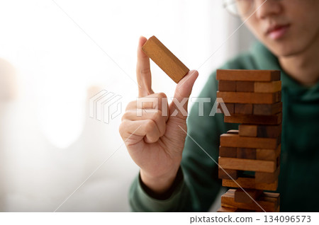Close up a man looking and holding a piece of wooden block in tower building game as playing alone. 134096573