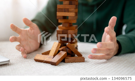 Close up a man's hands open palms aside pieces of wooden block in tower building game playing alone. 134096575