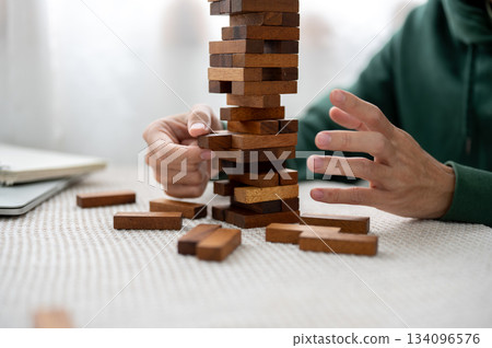 Close up a man's hand pulling out a pieces of wooden block in tower building game as playing alone. 134096576